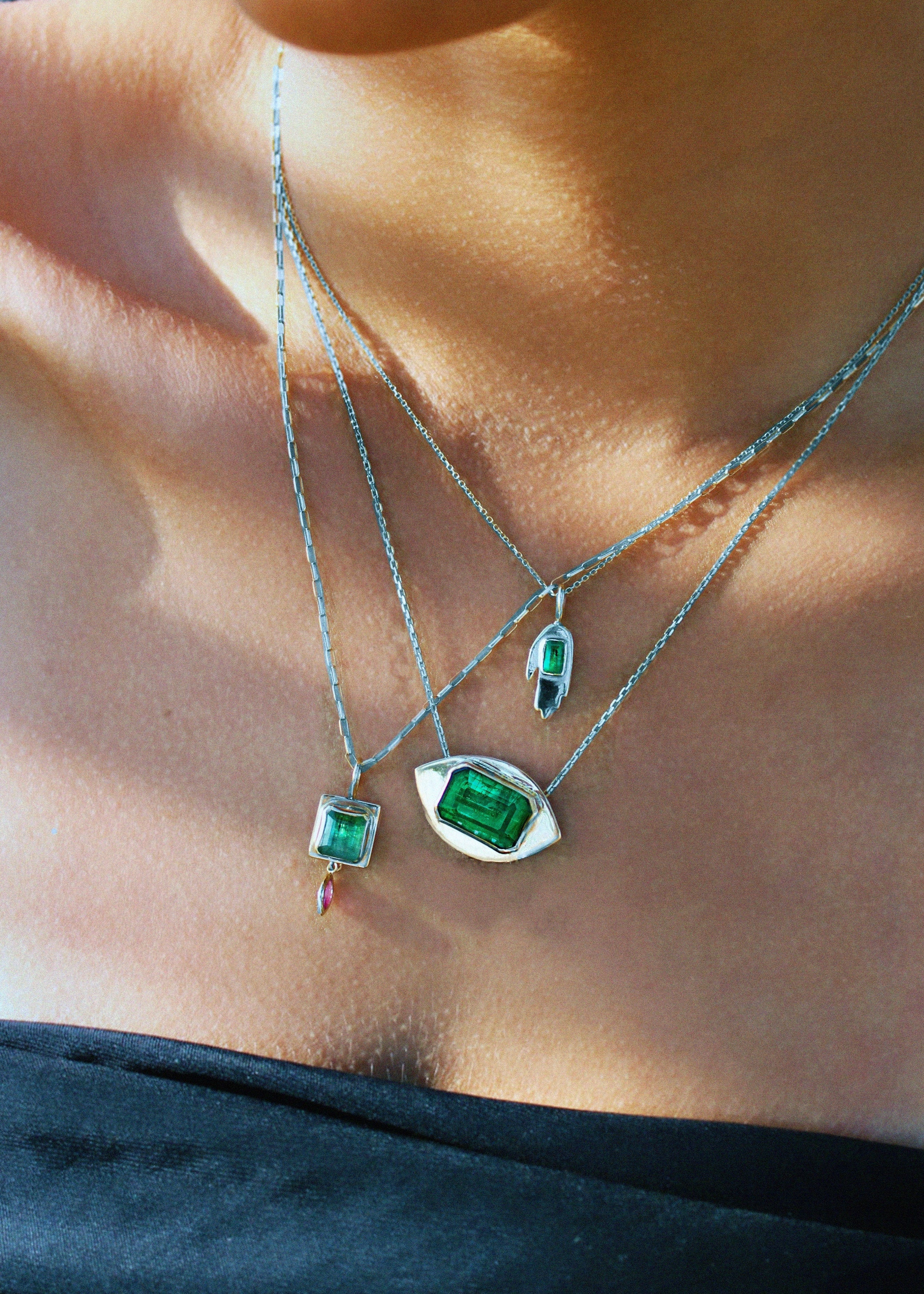 Close-up of a person wearing multiple necklaces with green gemstone pendants.