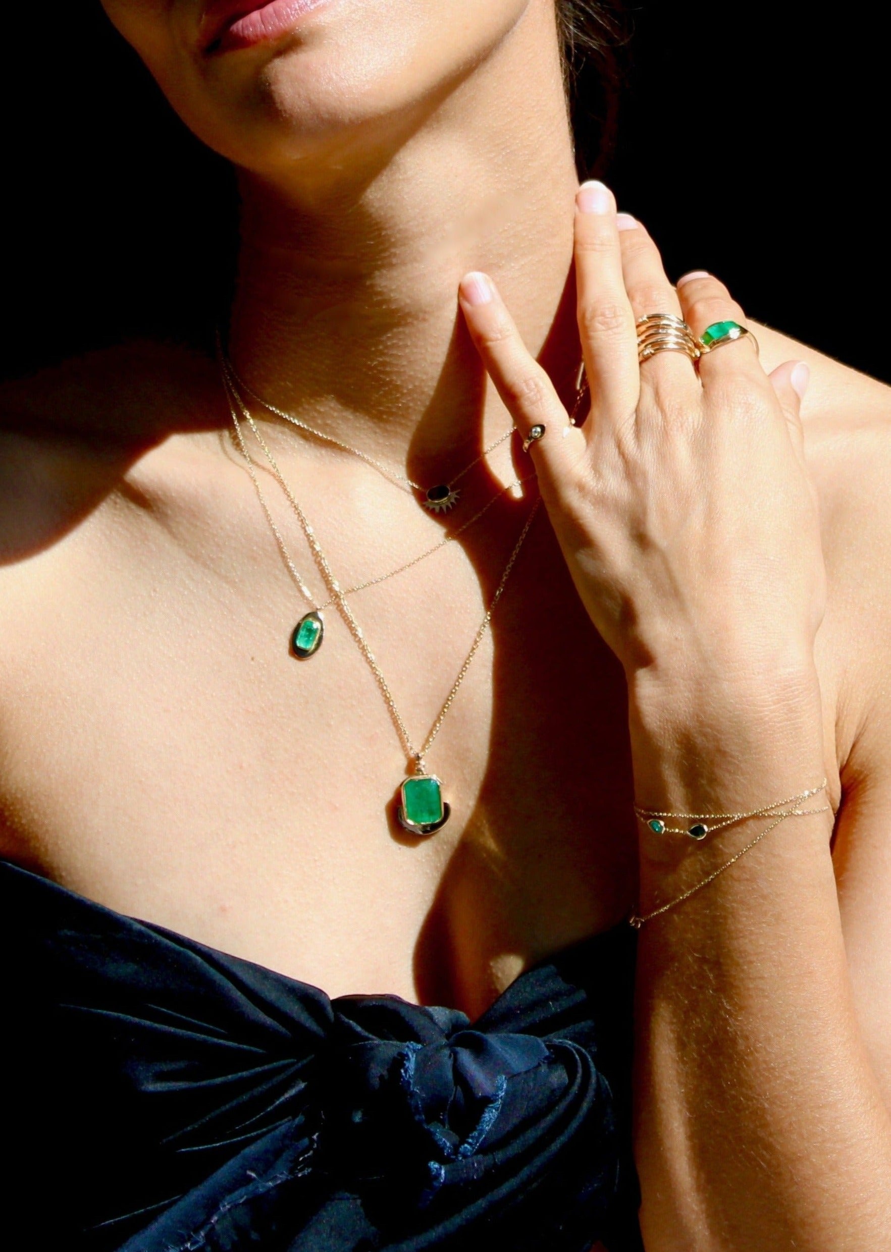 Chunky gold coin necklace with an emerald centerpiece on a long 20-inch chain, blending cultural heritage with modern elegance.