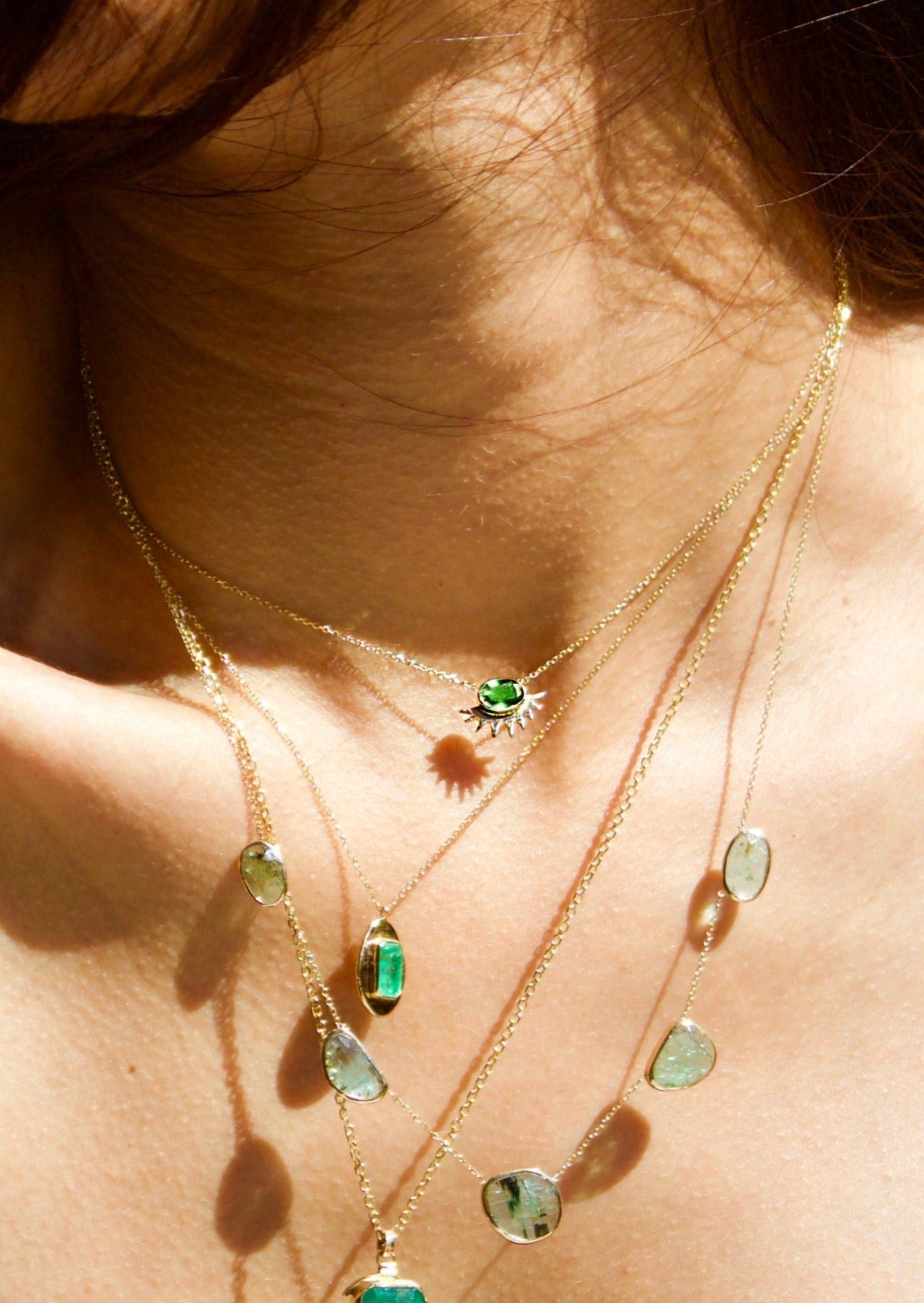 Dainty gold necklace stack featuring statement emerald jewelry pieces.