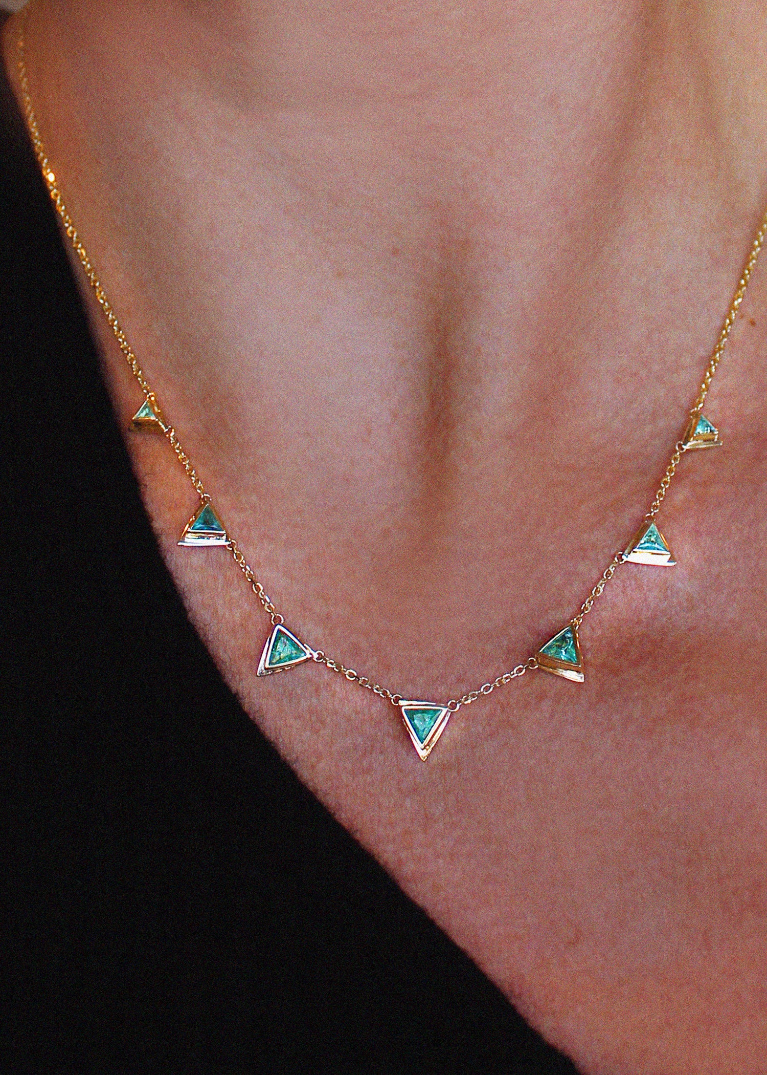 A 14K gold necklace featuring seven bezel-set emeralds in triangular stations along a delicate chain, perfect for everyday wear