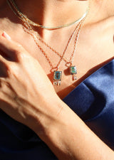 woman wearing rectangle shaped gold pendant with emerald and dangling diamonds