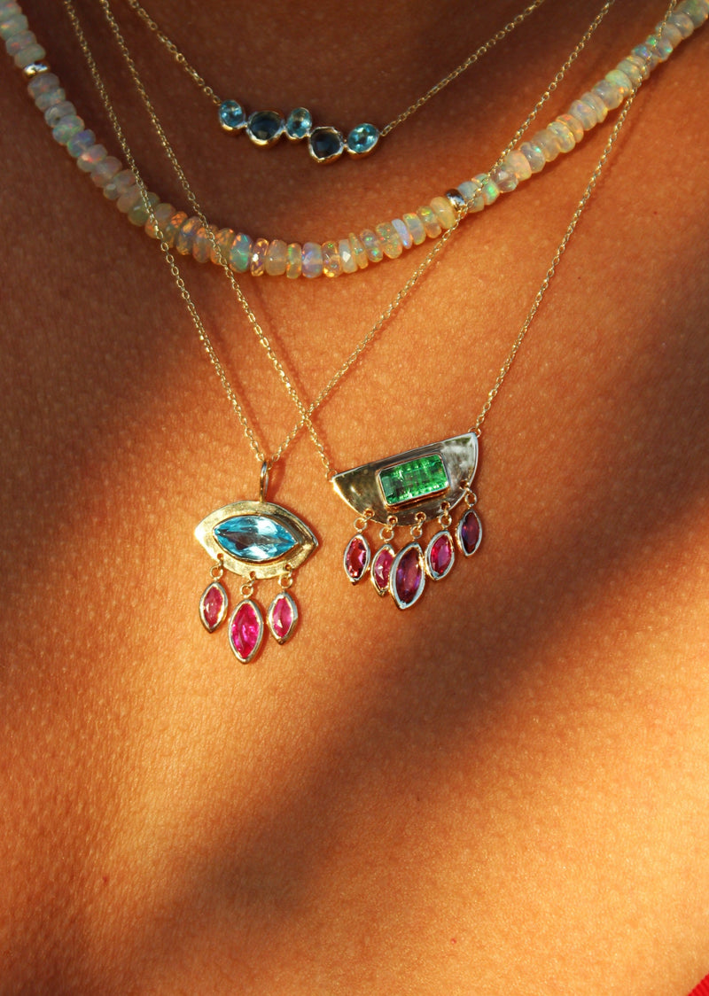 person wearing half moon pendant with center emerald and dangling rubies