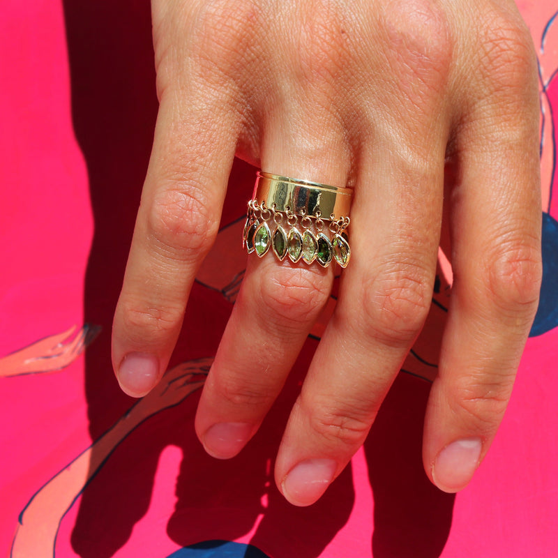 hand wearing ring with dangling green gems 